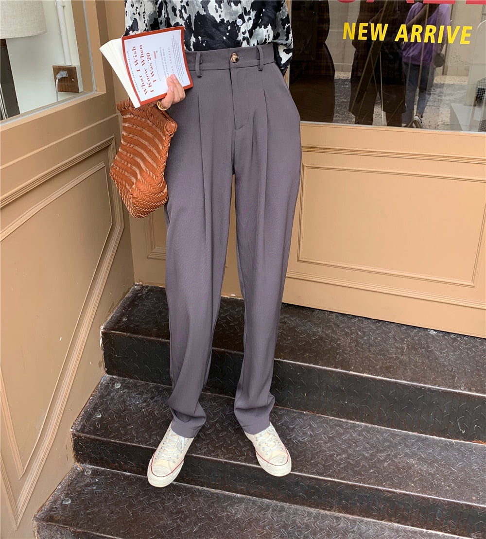 Model wearing Formal straight leg suit office trousers for women. Gray high waisted pleated trousers with sneakers and woven bag