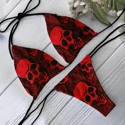 Red skull print bikini set with triangle cups and black string ties laid on white wood background