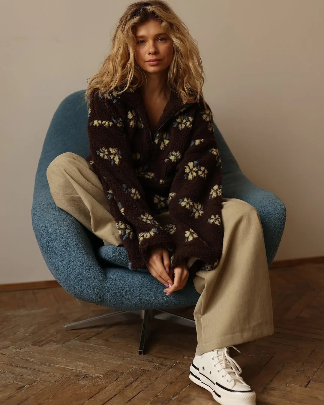 Chic model sitting in a blue chair wearing a cozy lambskin coat for women with floral patterns