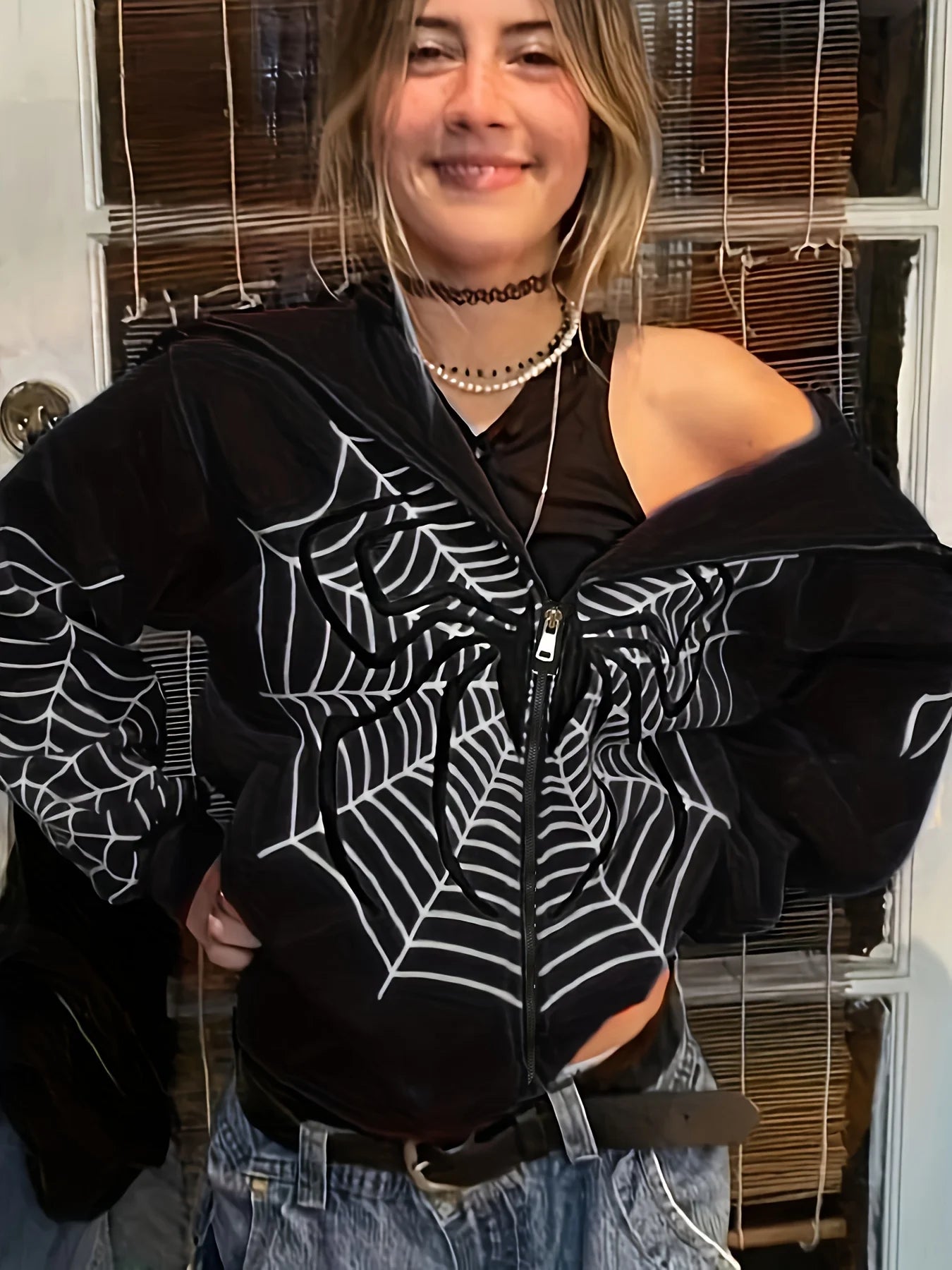 Model wearing black spider web zipper hoodie for women with white web print off shoulder style and jeans