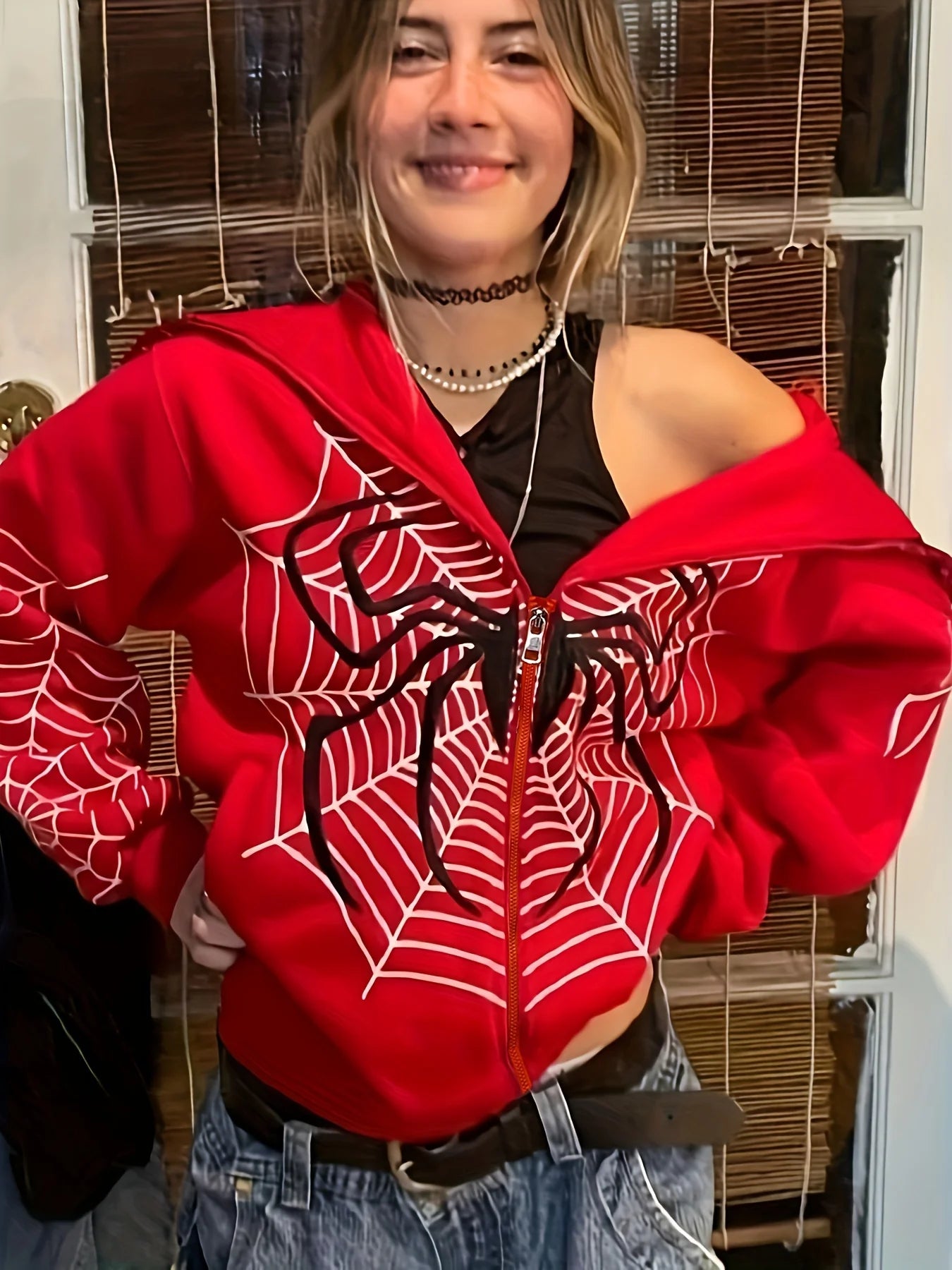 Model wearing red spider web zipper hoodie for women with front web graphic layered necklaces and jeans