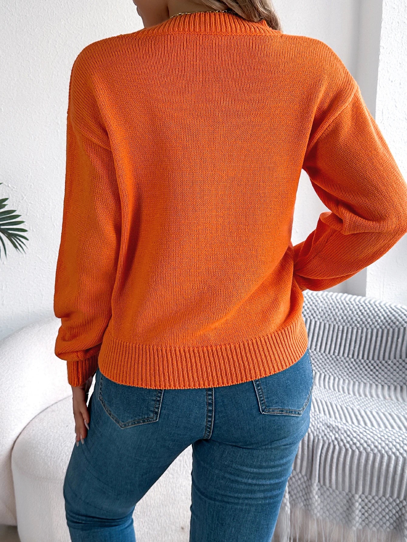 Back view of a cozy women's pumpkin sweater in bright orange, perfect for fall fashion