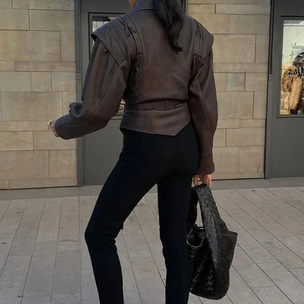 Back view of person wearing brown half collar faux leather jacket cropped with belt black pants and woven tote bag