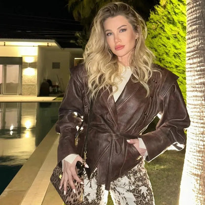 Blonde model wearing a brown half collar faux leather jacket with belt and patterned pants by pool