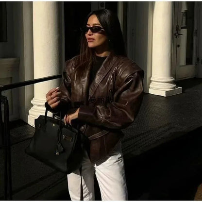 Woman wearing brown oversized half collar faux leather jacket styled with white pants and black handbag