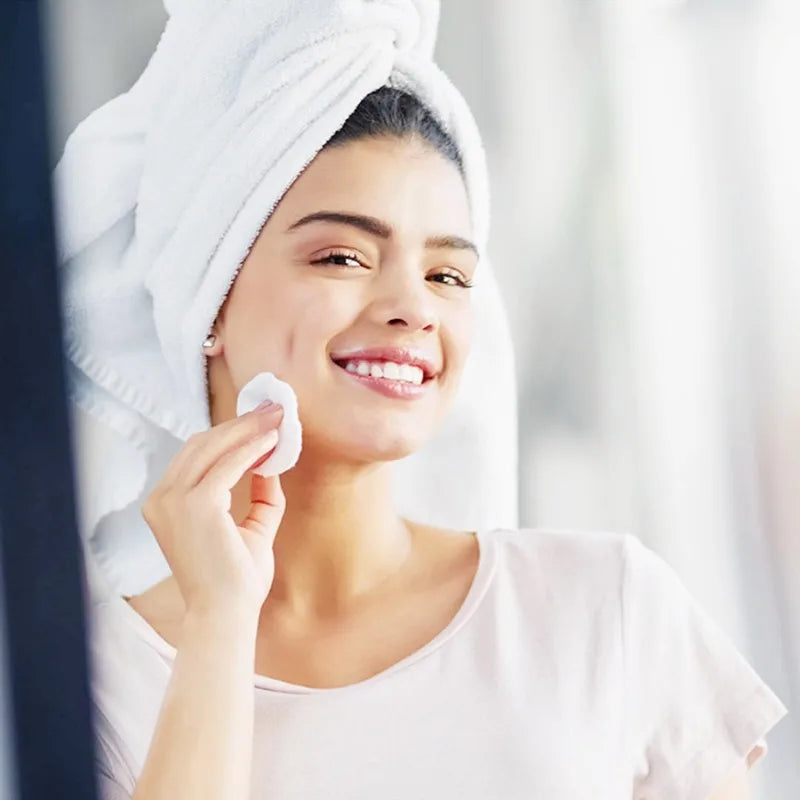 Woman using bamboo makeup remover pads reusable while smiling in a bathroom with a towel on her head
