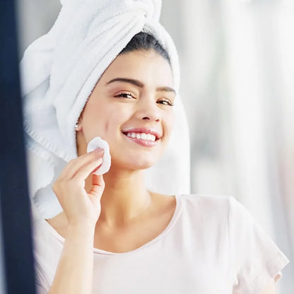 Woman using bamboo makeup remover pads reusable while smiling in a bathroom with a towel on her head