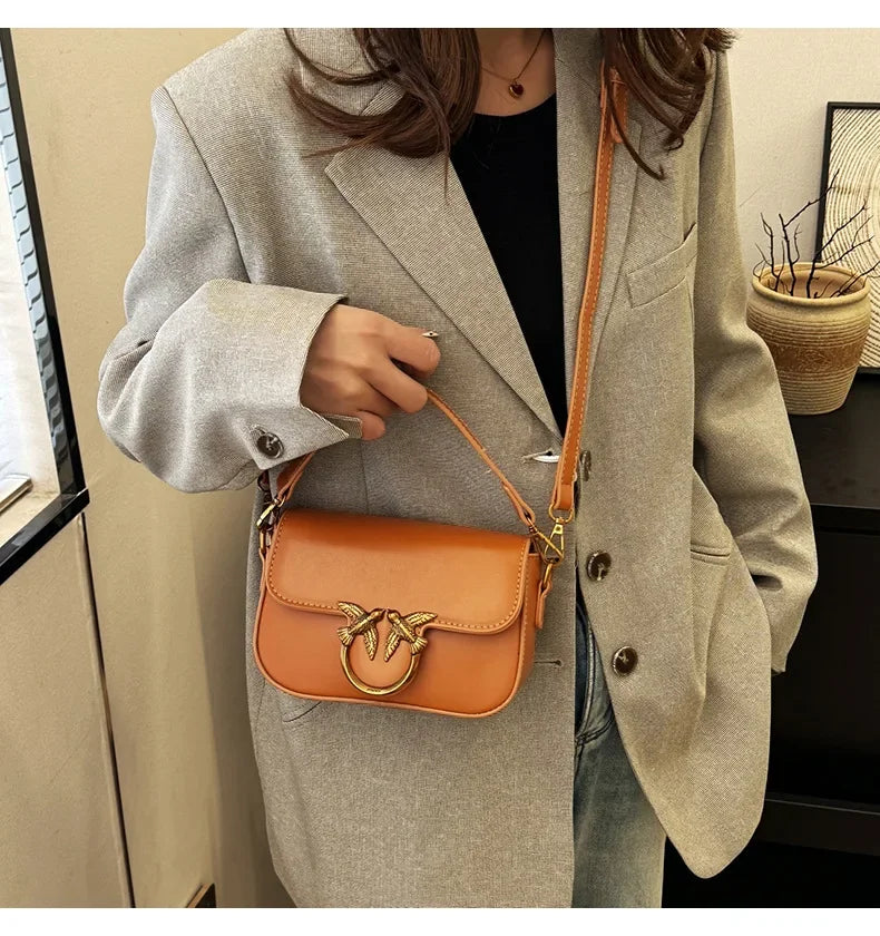 EtherealBe versatile small square tote bag in tan leather with gold bird clasp worn crossbody with gray blazer