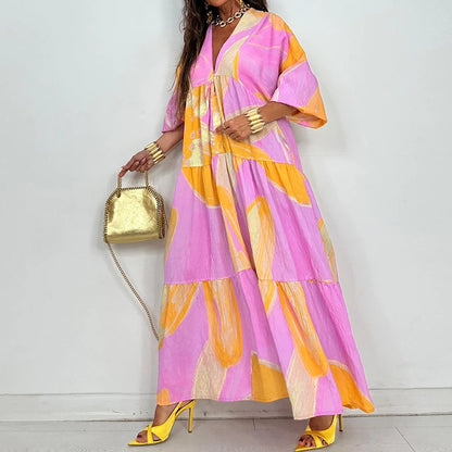 Model wearing elegant printed v-neck maxi dress in pink and yellow abstract print with gold handbag