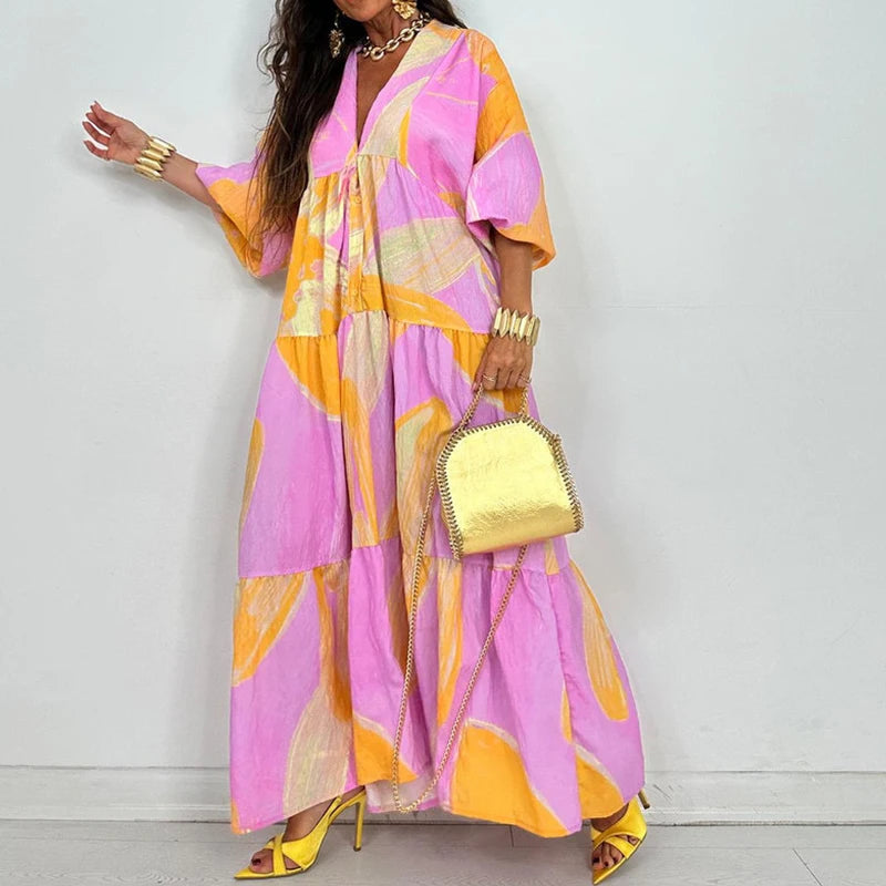 Model wearing EtherealBe elegant printed v-neck maxi dress in pink and yellow abstract print with tiered skirt and gold accessories