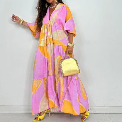 Model wearing EtherealBe elegant printed v-neck maxi dress in pink and yellow abstract print with tiered skirt and gold accessories