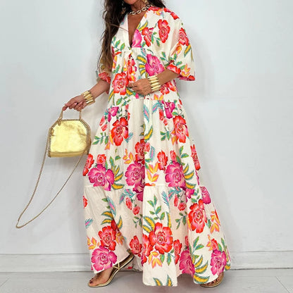 Model wearing elegant printed v-neck maxi dress in cream with bold pink floral print, tiered skirt, short sleeves and gold clutch