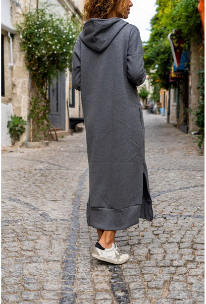 Model wearing a casual hooded V-neck dress in gray, walking on a cobblestone street