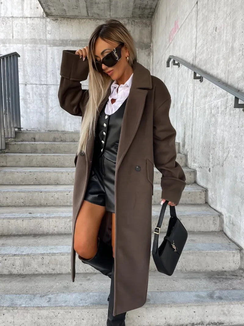 Model wearing elegant long coat for women in dark brown over white blouse and black leather shorts