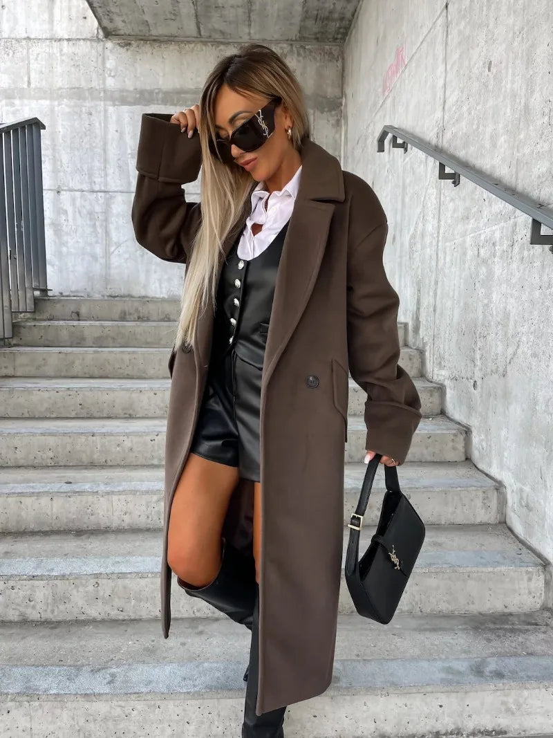 Woman modeling elegant long coat for women in dark brown over black leather outfit with knee boots and small black bag on stairs