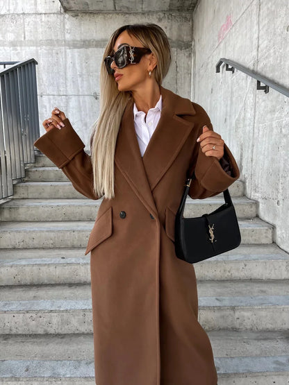 Model wearing a brown double breasted elegant long coat for women with white shirt black shoulder bag on concrete stairs
