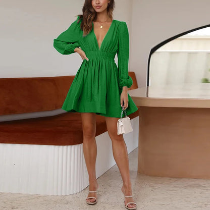 Green elegant v neck long sleeve mini dress on model with smocked waist holding white handbag and sandals