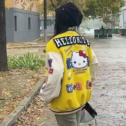 Back view of person wearing a yellow Hello Kitty baseball jacket with cream sleeves and patches walking on a tree lined sidewalk