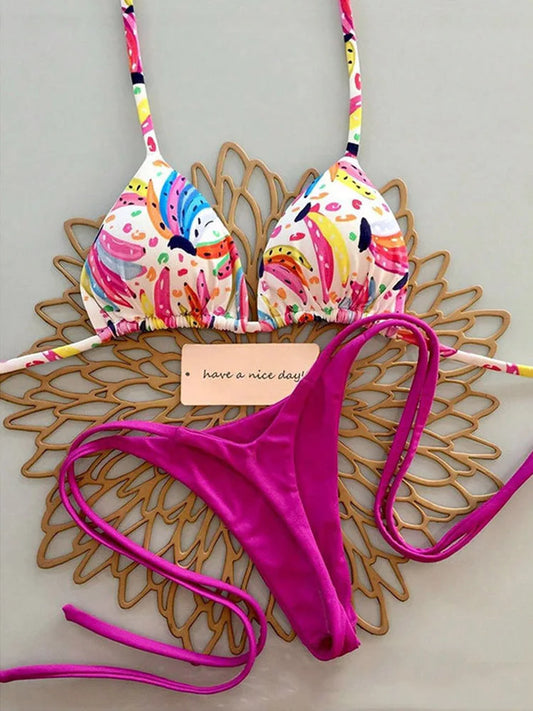 tropical fruit print bikini set with colorful triangle top and fuchsia string cheeky bottoms laid flat