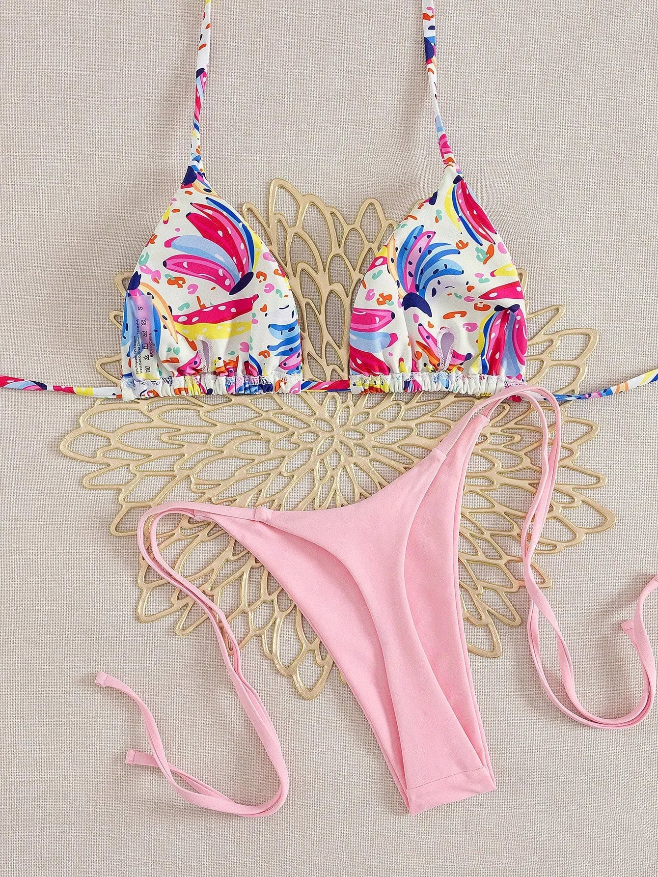 tropical fruit print bikini set with colorful triangle top and pink tie side cheeky bottoms on beige backdrop