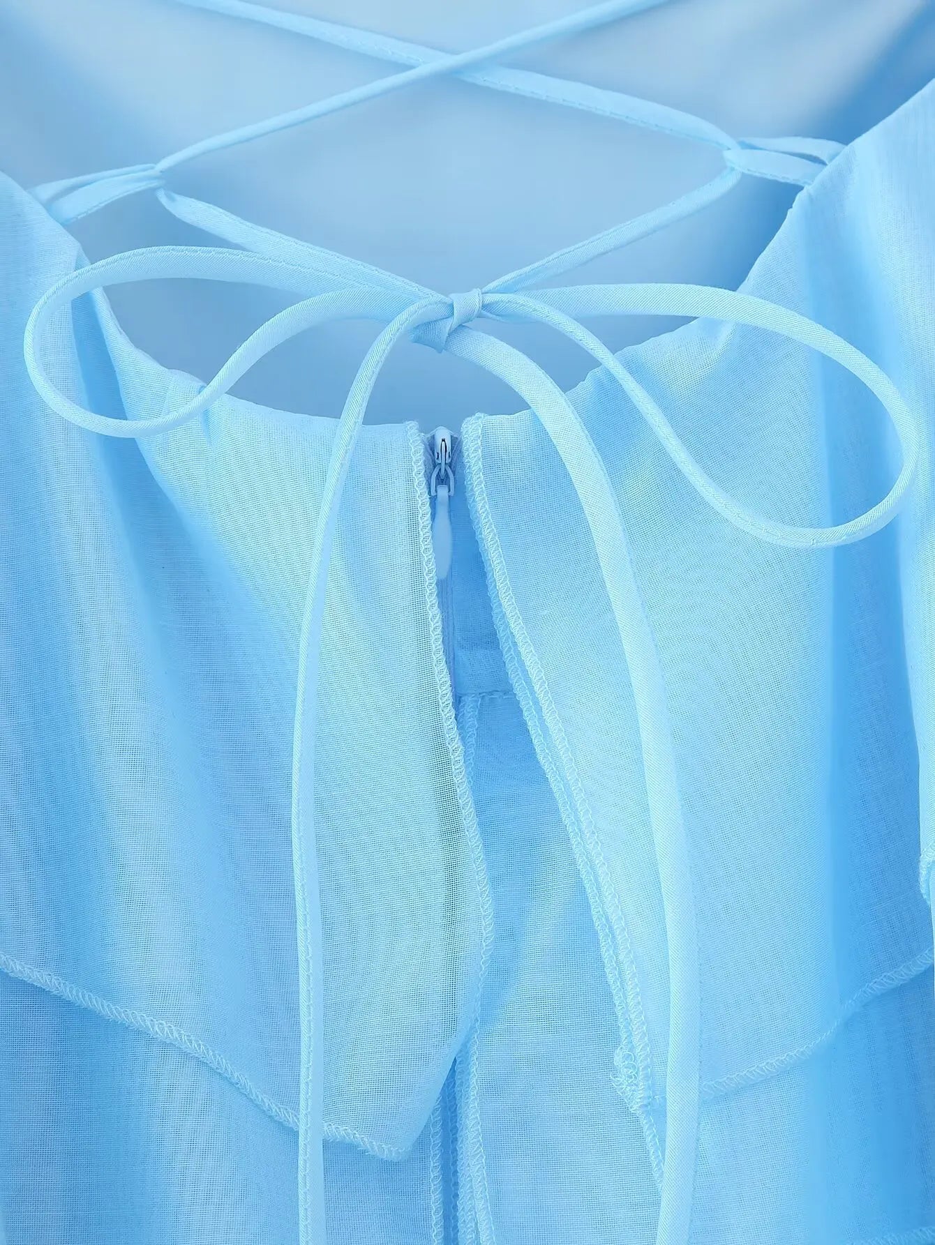 Back view of an elegant layered decorative dress showcasing delicate straps and a light blue color