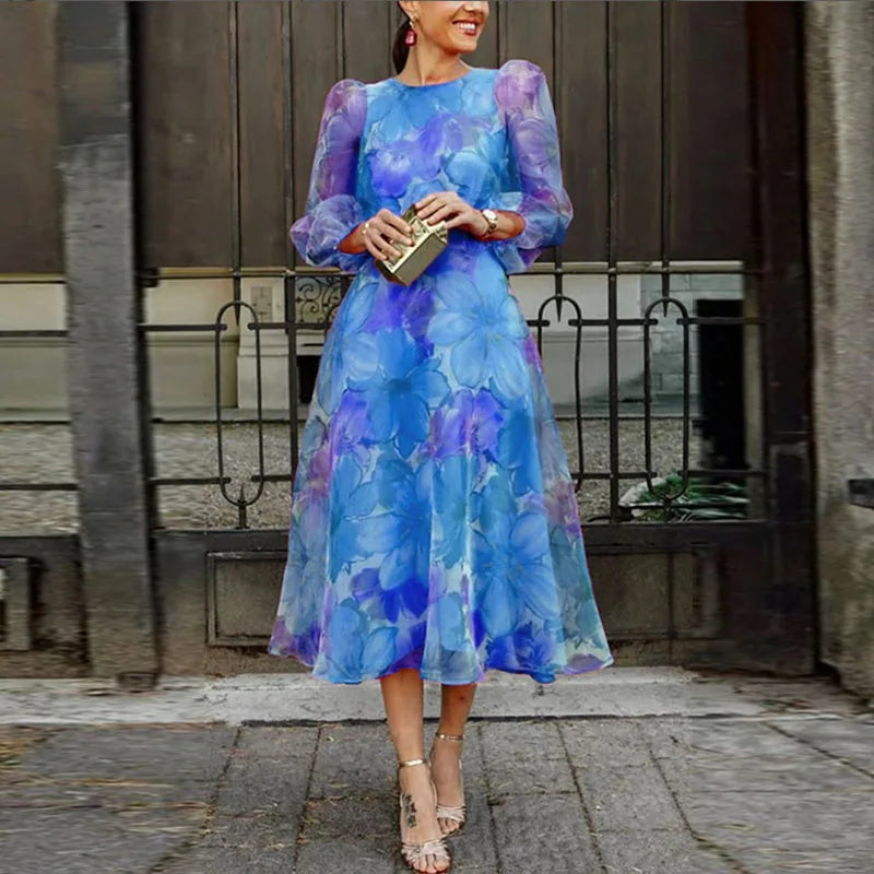 EtherealBe floral gauze evening dress in blue purple floral print midi with sheer puff sleeves and gold clutch