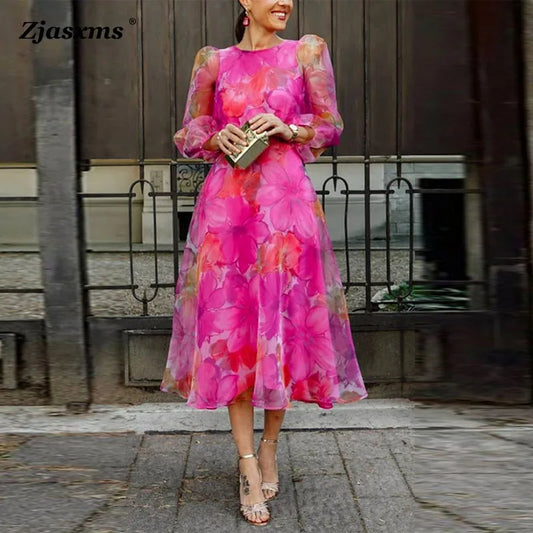 Woman wearing a pink floral gauze evening dress with sheer puff sleeves midi skirt holding gold clutch