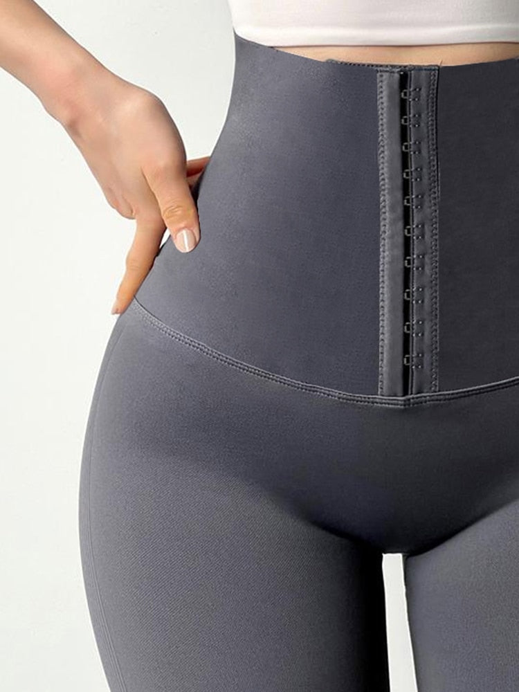 Gray fitness leggings with high waist tummy control and front hook closure on model adjusting waist