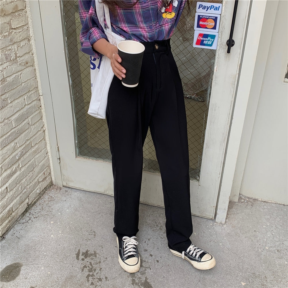 Woman wearing Formal straight leg suit office trousers for women in black high waist pleated front with sneakers holding coffee