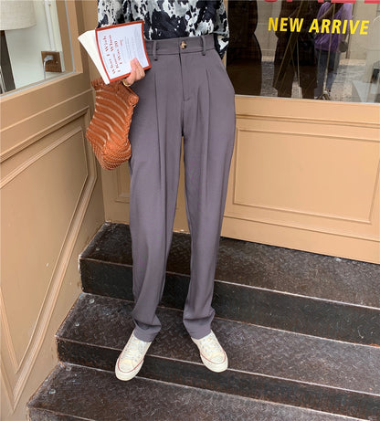 Model wearing Formal straight leg suit office trousers for women. Gray high waisted pleated trousers with sneakers and woven bag