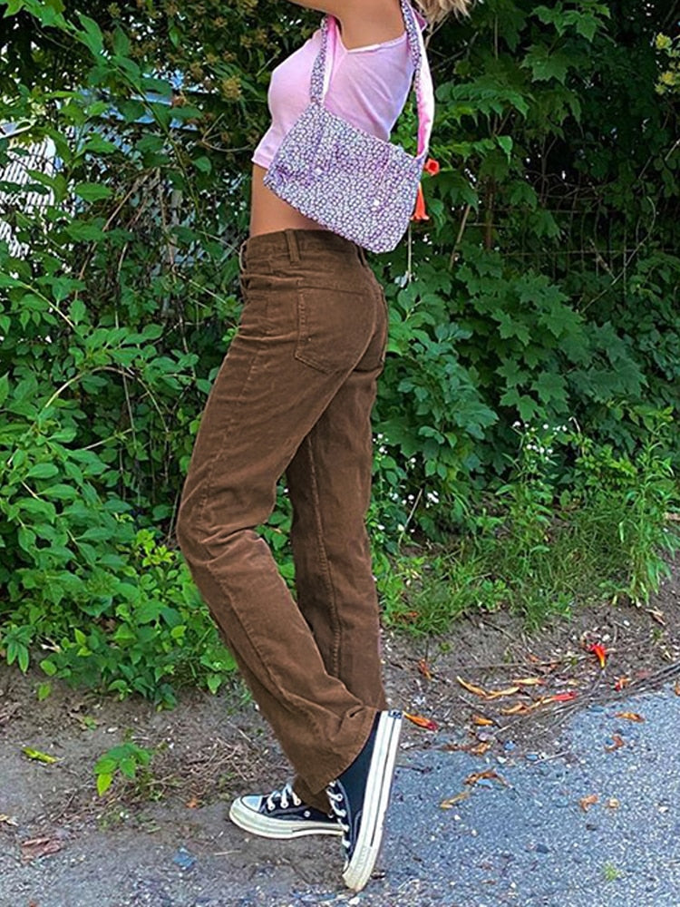 Model wearing brown thin corduroy pants for women with pink crop top floral shoulder bag and black sneakers