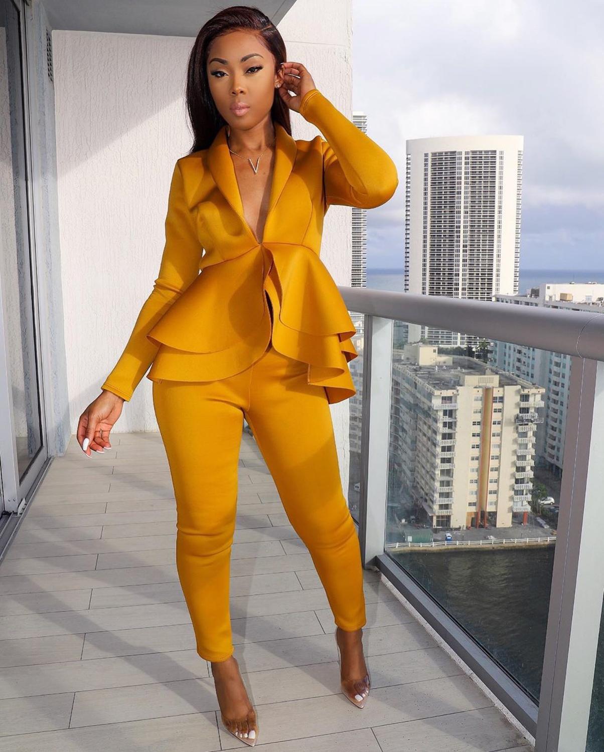 Model wearing mustard women ruffle blazer pants set with peplum ruffles and tapered pants on balcony