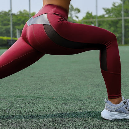 Woman in maroon high waist breathable sports leggings for gym with black mesh panels and white running shoes on turf