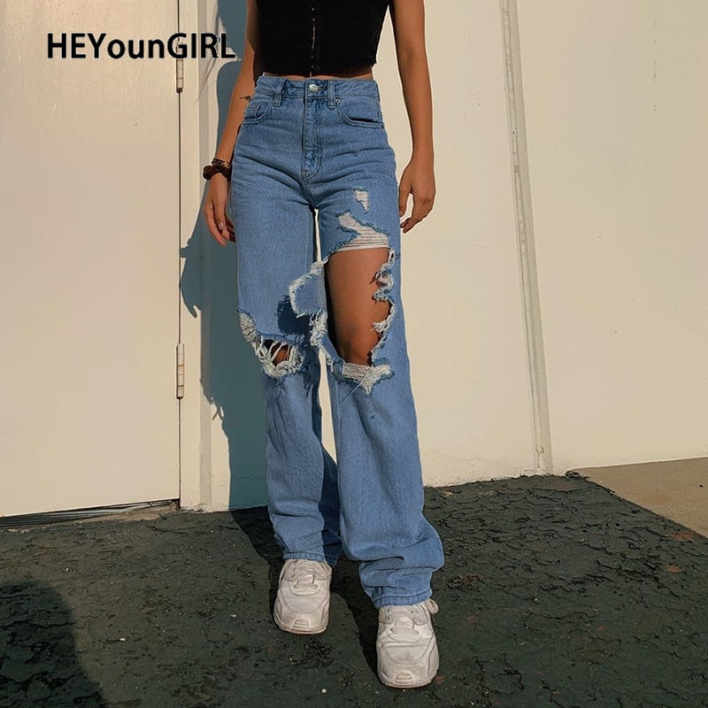 Model wearing high waist hollow out ripped denim pants in light blue with large thigh and knee cutouts and white sneakers