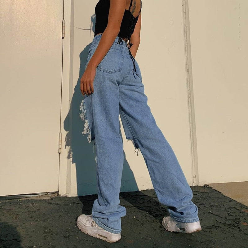 Model wearing hollow out ripped denim pants in light blue with side distressing paired with black crop top and white sneakers