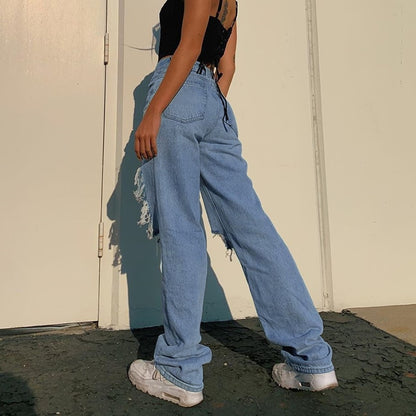 Model wearing hollow out ripped denim pants in light blue with side distressing paired with black crop top and white sneakers