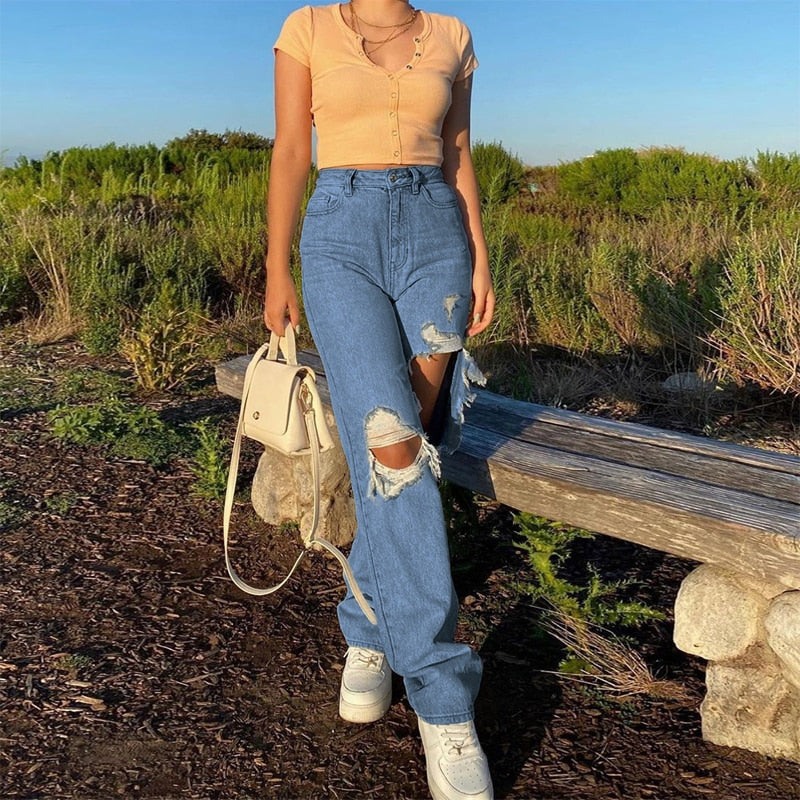 Model wearing hollow out ripped denim pants high waist blue with knee cutouts beige crop top and white sneakers