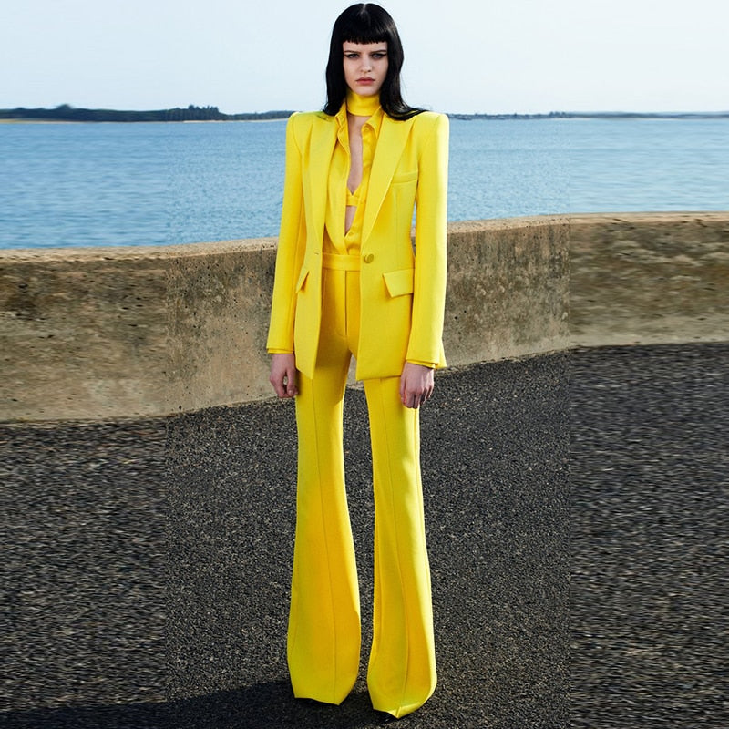 Model wearing bright yellow tailored flare pants blazer set for women with high waisted flares and structured blazer by the sea