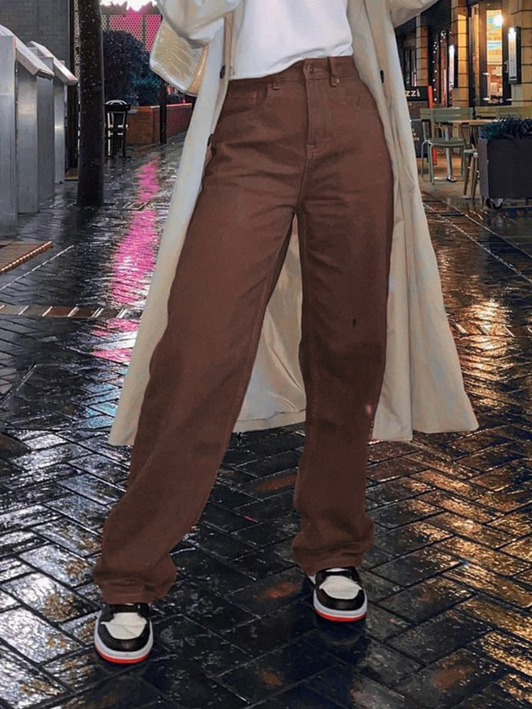 Model wearing brown vintage high waist wide leg pants with sneakers and long trench coat on wet city street