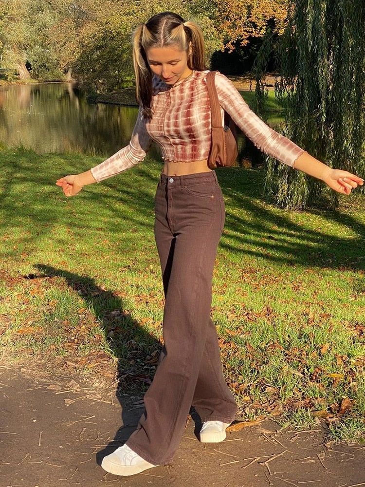 Woman wearing brown vintage high waist wide leg pants with white sneakers and tie dye crop top in park