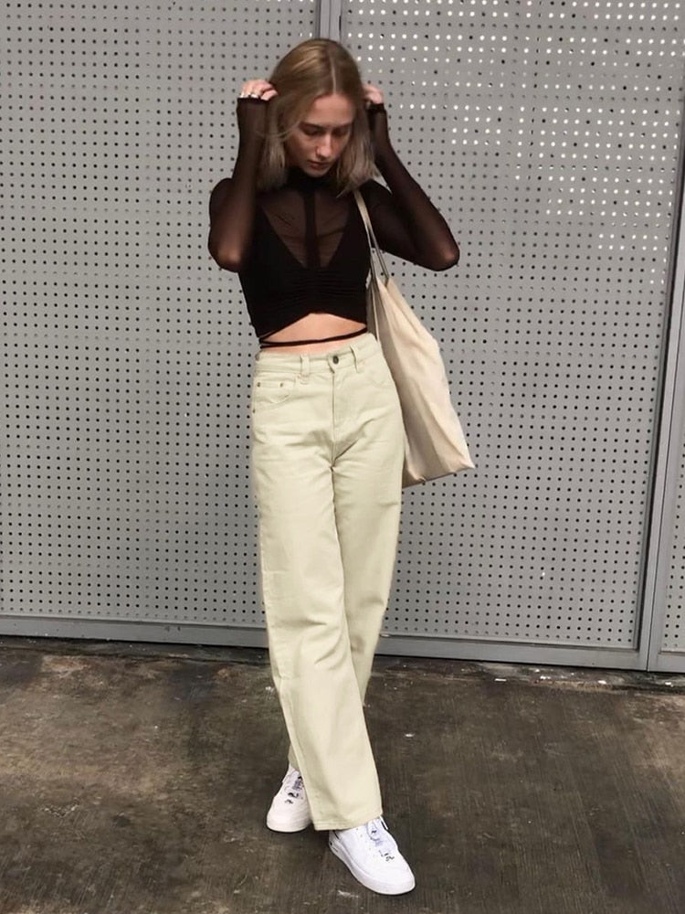 Model wearing vintage high waist wide leg pants in cream with black sheer crop top white sneakers tote