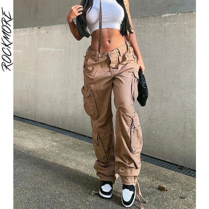 Model wearing women's low waist cargo jeans in tan with multiple pockets tied ankles and white crop top