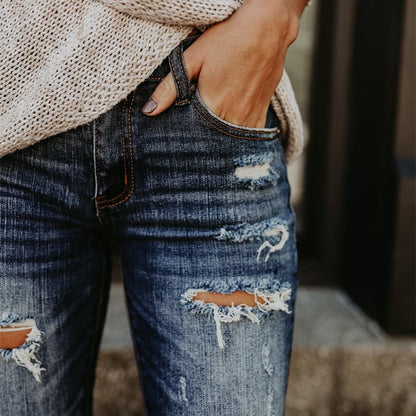 Closeup of dark wash boyfriend ripped jeans for women with knee distressing and hand in pocket