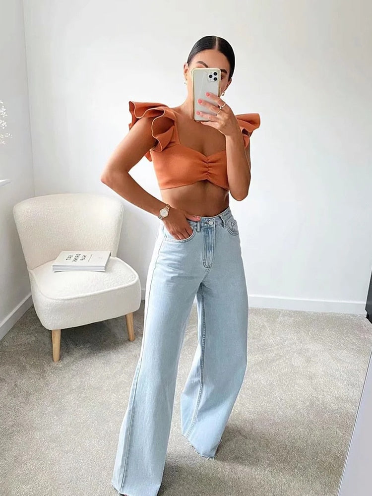 Model wearing womens straight leg high waist jeans paired with a stylish orange top in a modern interior