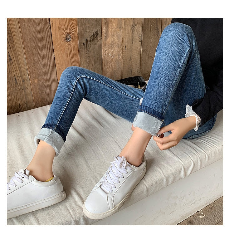 Woman sitting on bench in cuffed blue denim fleece lined skinny jeans for women with white sneakers